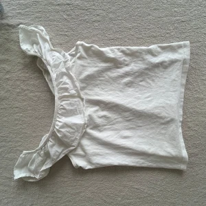 Vit topp från Holly & White - Säljer en söt vit topp från Holly & White i storlek XS. Toppen har volangdetaljer vid axlarna och är ärmlös, perfekt för varma dagar. Materialet är mjukt och bekvämt.