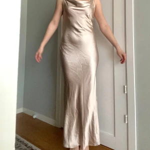 Beige satinklänning  - Jättefin lång klänning i champagne färg med låg rygg och justerbara axelband. Jag hade denna på min studentbal men är lika fin att ha i sommar.