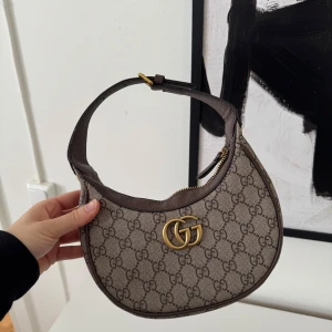 Mönstrad axelväska med gulddetaljer - Snygg axelväska med ett klassiskt mönster och gulddetaljer. Väskan har en dragkedja upptill och ett justerbart axelband. 