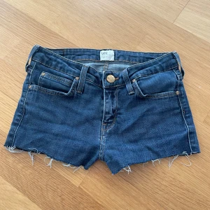 Jeansshorts från Lee - Säljer ett par snygga jeansshorts från Lee med fransiga kanter och jättefina detaljer på fickorna. Märket som sitter ovanför rumpan är lite sprucken. 