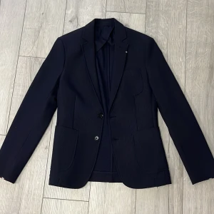 Kavaj  - Elegant svart kavaj från Zara Man med två knappar framtill. Kavajen har en klassisk design med smal passform och är perfekt för formella tillfällen. Den är tillverkad i ett material som ger en stilren look.