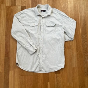 Vit skjorta från Morris - Säljer en stilren vit skjorta från Morris i storlek M. Skjortan har långa ärmar och två bröstfickor med knappar. Den är tillverkad i ett mjukt bomullsmaterial och har en broderad detalj på fickan. Perfekt för en avslappnad look.