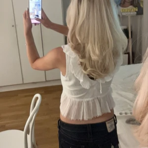 Vit ärmlös blus med volangdetaljer - Säljer en söt vit ärmlös blus med volangdetaljer och knytning i ryggen