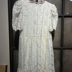 Vit studentklänning - Charmig vit klänning från & other stories med vackert broderat mönster. Klänningen har korta ärmar och en volangdetalj vid fållen. Perfekt för en somrig look!