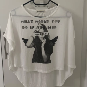 Vit t-shirt med tryck från Jurianojurrie - Cool vit t-shirt med ett svartvitt tryck av en person med vingar och texten 'What would you do if you bird oh shit!'. T-shirten har en lös passform och korta ärmar, perfekt för en avslappnad stil.