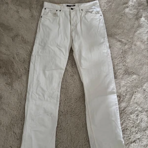 Vita jeansbyxor från Tommy Hilfiger - Snygga vita jeansbyxor från Tommy Hilfiger med klassisk femficksdesign och knappgylf. Byxorna har en rak passform och är perfekta för en stilren look. Märkeslogga på bakfickan och läderpatch vid midjan.