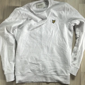 Vit tröja från Lyle & Scott - Säljer en stilren vit tröja från Lyle & Scott med deras ikoniska logga på bröstet. Tröjan är långärmad och tillverkad i ekologiskt material. Perfekt för en avslappnad look.