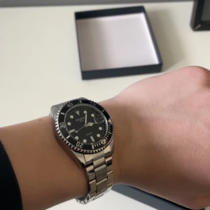 Silverfärgad klocka  - Snygg och stilren klocka med silverfärgad länk och svart urtavla. Klockan har tydliga markeringar och en vridbar bezel. Perfekt för den som gillar en klassisk look. Klockan är helt ny och oanvänd.