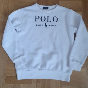 Vit sweatshirt från Ralph Lauren - Säljer en stilren vit sweatshirt från Ralph Lauren med det klassiska Polo-logotypen tryckt på framsidan. Tröjan har långa ärmar och ribbade muddar vid ärmslut och nederkant. Perfekt för en avslappnad och snygg look.