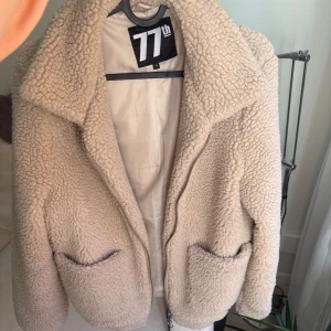 Beige teddyjacka - Beige teddyjacka från 77th med dragkedja framtill och två fickor. Jackan är tillverkad i 100% polyester och har en skön, fluffig textur.