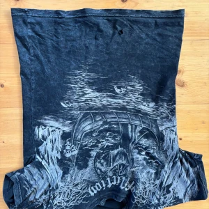 Svart t-shirt från Affliction - Cool svart t-shirt från Affliction med ett stort tryck i grått på framsidan. T-shirten har en normal passform och korta ärmar. Perfekt för dig som gillar en rockig stil. 🖤