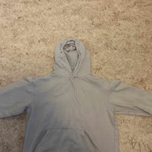 Ljusgrå hoodie från H&M Essentials - Säljer en ljusgrå hoodie från H&M Essentials. Den har en avslappnad passform med en justerbar huva och en stor magficka framtill. Perfekt för en casual look.