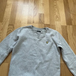 Grå sweatshirt från Lyle & Scott - Säljer en stilren grå sweatshirt från Lyle & Scott med deras ikoniska logga broderad på bröstet. Tröjan har en rund halsringning och långa ärmar med ribbade muddar. Säljer min brors tröja💓jätte fint skick! 