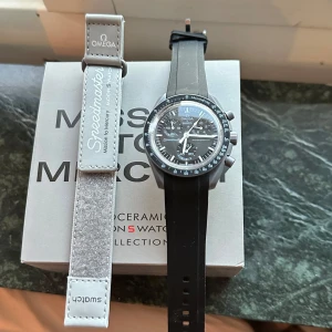 Omega x Swatch Speedmaster - Säljer en Omega x Swatch Speedmaster med svart urtavla och svart armband. Klockan har en klassisk design med tydliga markeringar och en stilren look. Perfekt för den som gillar tidlös elegans.