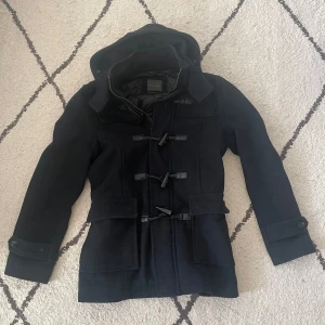 Navy cardigan från Zara Man - Snygg navy cardigan från Zara Man med huva och knäppning framtill. Jackan har långa ärmar och praktiska fickor. Perfekt för kyligare dagar.