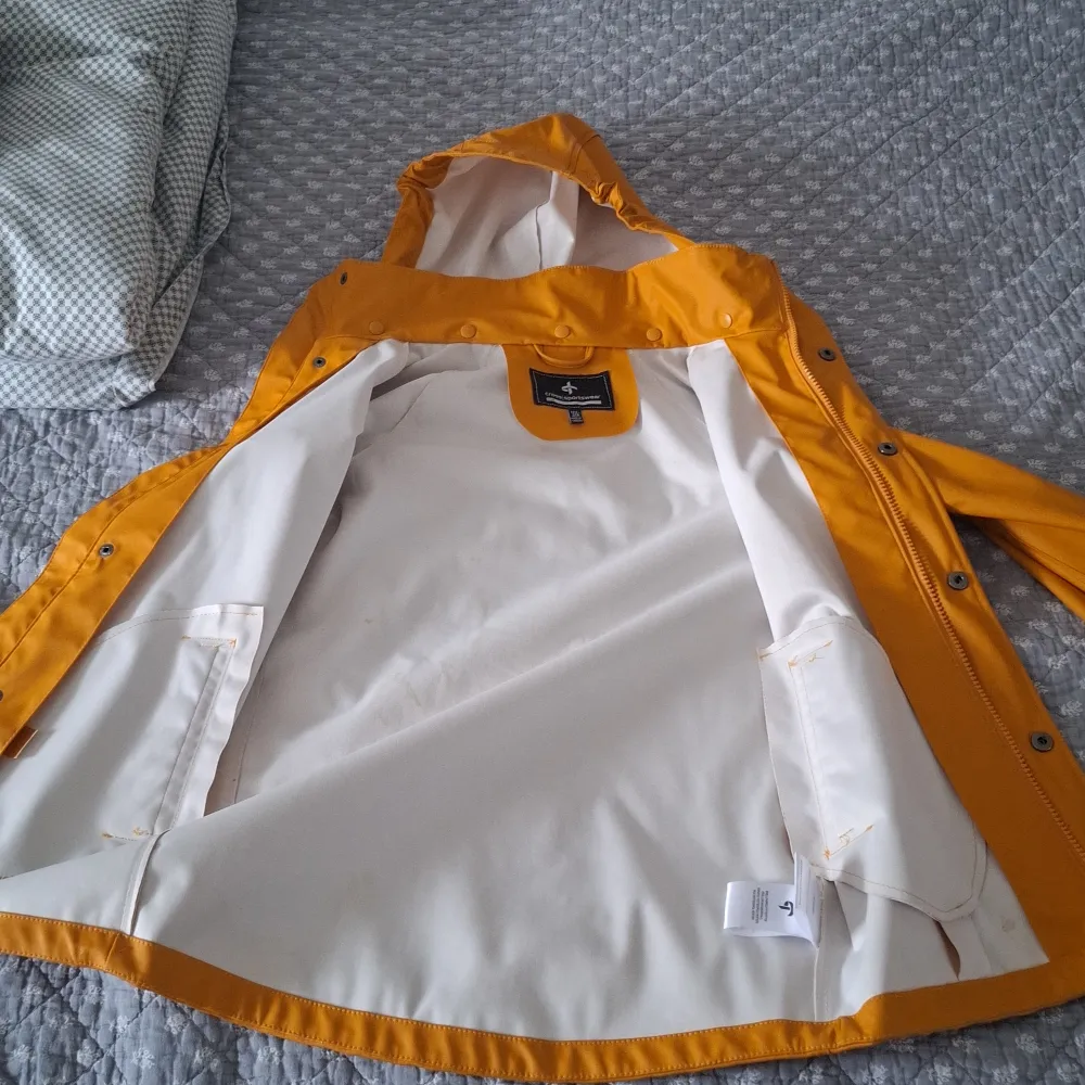 Säljer en snygg gul regnjacka från Cross Sportswear. Jackan har en huva och stängs med knappar och dragkedja. Perfekt för regniga dagar och håller dig torr och bekväm. Den har en vit insida och praktiska fickor framtill. Har några få fläckar, knappast märkbara . Takit.