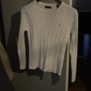 Vit stickad tröja från GANT - Säljer en stilren vit stickad tröja från GANT med kabelstickat mönster. Tröjan har långa ärmar och en rund halsringning. Perfekt för en klassisk och tidlös look.