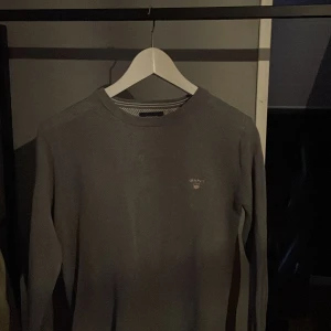Grå tröja från GANT - Säljer en stilren grå tröja från GANT i premium bomull. Tröjan har en diskret logga på bröstet och är perfekt för en avslappnad look. Den har långa ärmar och en klassisk rund halsringning.
