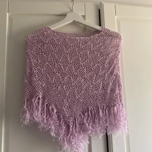 Ljuslila virkad  poncho med paljetter - Säljer en ljuslila virkad poncho med glittrande paljetter och fransar längs nederkanten.