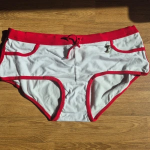 Vit och röd trosa med Snoopy M - Snygg vit trosa med röda detaljer och en tecknad Snobben på baksidan. Tillverkad i 95% bomull och 5% elastan för en bekväm passform. Helt ny med orginaletiketterna kvar.  Se också mina andra annonser för möjlighet till paket/bundle med rabatt och samfrakt. För dyrt för dig? Kom med ett bud.