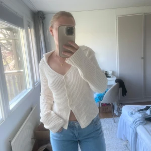 Topp NAKD  - Säljer en stilren vit ribbad kofta med knappar framtill. Koftan har långa ärmar och en v-ringad design som ger en klassisk look. Perfekt för att hålla sig varm och snygg under kyligare dagar.