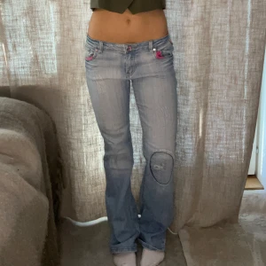 Ljusblå jeans med rosa detaljer - Säljer ett par ljusblå jeans med rosa detaljer på fickorna. Byxorna har en bootcut-stil och är lågmidjade. Perfekta för en avslappnad look.