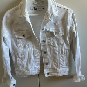 Vit jeansjacka från Zara - Säljer en stilren vit jeansjacka från Zara i storlek XS. Jackan har knappar framtill och två bröstfickor med lock. Perfekt för vår och sommar!