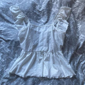 Vit topp med volangdetaljer -  Vit topp med fina volangdetaljer på axelbanden och en söt knytning i ryggen från Shein. Väldigt luftig och perfekt på sommaren till olika tillfällen