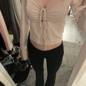 Beige långärmad topp med knyt - Säljer en beige långärmad topp med knyt framtill. Toppen har en v-ringad design och är tillverkad i ett mjukt material. Perfekt för en stilren look. har två minifläckar som man ser på bild 3💞