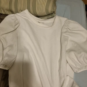 Vit blus med puffärmar - Säljer en stilren vit blus med puffärmar. Perfekt för en elegant look. Blusen har en rund halsringning och är tillverkad i ett lätt material.