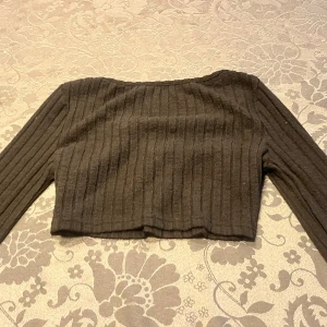 Svart och lila ribbad croppad topp - Säljer två snygga ribbade croppade toppar. Den ena är svart och den andra är lila med en söt rynkad detalj framtill. Båda har långa ärmar och en stilren design. Perfekta för att styla med jeans eller kjol!