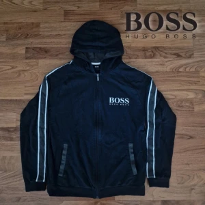 Hugo Boss Hoodie - Säljer en snygg hoodie från Hugo Boss i storlek S och i nyskick dessutom! Den har en dragkedja framtill och en huva för extra komfort. Perfekt för höst och vår, med vita detaljer längs ärmarna som ger en sportig look. Snabb leverans - Skickas samma dag📦 Kontakta mig gärna vid intresse eller funderingar!📌