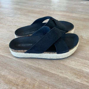 Svarta sandaler från Topway - Snygga svarta sandaler från Topway med korsade remmar och en bekväm platt sula.  Sulan har en stilren design med en naturfärgad kant.