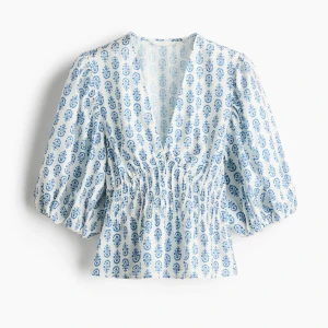 Blåvit blus med puffärm och v-ringning - Superfin blus i vitt med blått blommönster, djup v-ringning och smockad midja. Använd 1 gång. Inga defekter, som ny 