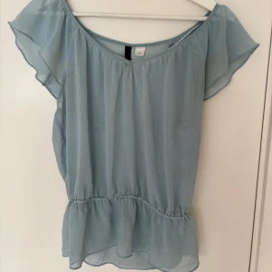 Ljusblå blus med volangärm - Söt ljusblå blus i tunnt och luftigt material med volangärmar och resår i midjan som ger en fin form. Blusen har en lätt transparent känsla och en feminin, flowy siluett🩷
