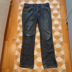 Nudie Jeans blå jeans W34 L34 - Säljer ett par klassiska blå jeans från Nudie Jeans i rak modell. Jeansen har snygga kontrastsömmar och Nudie-logga på bakfickan. Tillverkade i slitstarkt denimtyg och passar perfekt till en avslappnad stil.