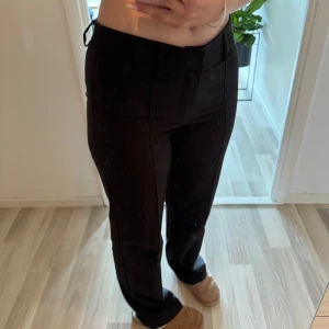 Svarta kostymbyxor från Madlady - Svarta kostymbyxor från Madlady med raka ben och hög midja. Byxorna har pressveck framtill, bälteshällor och stängs med dragkedja och två knappar. 