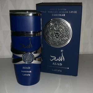 Lattafa Asad Zanzibar  - Lattafa Asad Zanzibar är en parfym i en stilren, djupblå flaska med silverdetaljer och orientaliskt mönster. Flaskan har en robust, modern design och levereras i en matchande blå kartong med silverlejon och arabiska inslag. Perfekt för dig som gillar exklusiva dofter. 95ml/100ml
