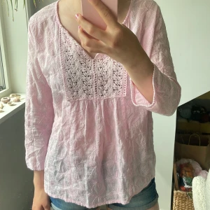 Ljusrosa blus med broderi från Dotted Blue - Supersöt ljusrosa blus från Dotted Blue med broderade detaljer och spets framtill. Blusen har trekvartsärm och v-ringning. Det står att det är storlek 42 men skulle säga att det är mer en 34-36 eller typ xs-S