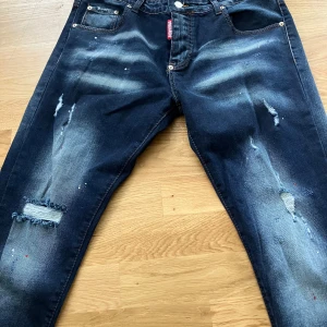 Mörkblå distressed jeans från Dsquared2 - Snygga mörkblå jeans från Dsquared2 med slitna detaljer, fransade hål. Klassisk femficksmodell med Dsquared2-logga bak. Jeansen har en modern passform och är perfekta för en trendig streetstyle-look.