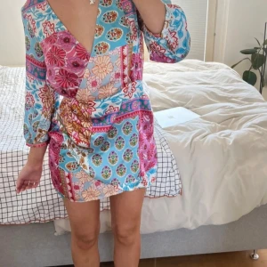 Färgglad omlottklänning från Zara - Säljer en färgglad omlottklänning från Zara med blommigt mönster i blått, rosa, rött och beige. Klänningen har trekvartsärm och v-ringning, samt resår i midjan för en bekväm passform. Perfekt för dig som gillar bohemisk stil! Ny oanvänd 