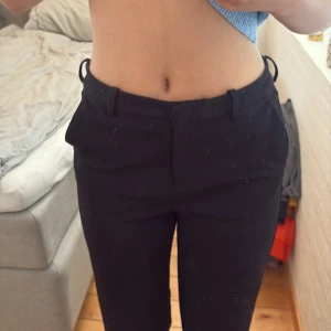 Svarta kostymbyxor från Vero Moda - Snygga svarta kostymbyxor från Vero Moda med klassisk rak passform och hällor för bälte. Byxorna har diskreta fickor i sidorna och byxorna stängs med dragkedja och knapp. Perfekta till en stilren look och enkla att matcha med olika toppar. Köpare står för frakt!💞