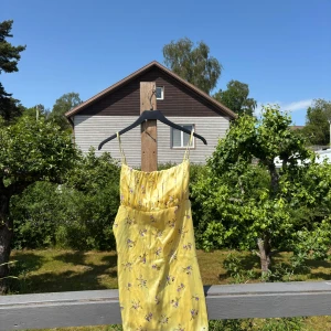 Gul blommig sommarklänning från ASOS - Gul klänning med lila blommor från asos. Använd en midsommar. Står som storlek 44 men jag som är S har använt den utan att det sett något konstigt ut!