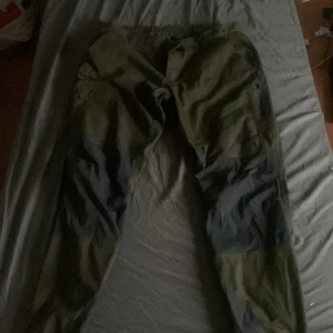 Gröna cargopants med grå detaljer  - Säljer ett par gröna cargopants med grå förstärkningar på knän och bak. Byxorna har flera fickor på sidorna och elastisk midja för extra komfort. Perfekta för dig som gillar en avslappnad och funktionell stil.