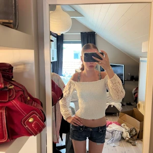 Vit hollister offshoulder topp med spetsärmar - Supersöt vit hollister offshoulder topp med croppad passform och långa, transparenta spetsärmar. Smockad överdel som sitter tajt och ger en snygg siluett. Perfekt för dig som gillar romantiska vibes och vill sticka ut lite extra. på lappen står det storlek medium men jag skulle säga att den sitter som en small