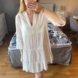 Vit kortklänning med volanger - Superfin vit kortklänning i boho-stil med v-ringning och trekvartsärm. Klänningen har flera volanglager och är tillverkad i ett lätt och luftigt tyg. Klänningen är från Vero Moda i storlek S. Jag säljer den eftersom den inte längre används av mig. Hör av dig vid frågor🫶🏽☺️