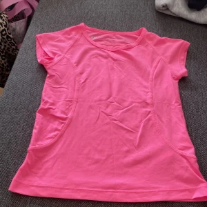 Rosa sporttopp från H&M - En riktigt snygg och sportig rosa topp från H&M Sport. T-shirten har korta ärmar, rund halsringning och är gjord i ett lätt och stretchigt syntetmaterial som passar perfekt för träning. Snygga sömdetaljer längs sidorna ger en cool look.