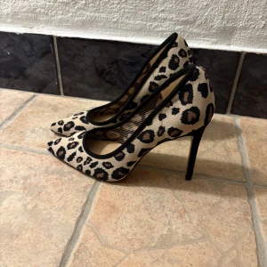 Leopardmönstrade klackar - Snygga pumps med leopardmönst.Skorna har spetsig tå, hög klack och svarta detaljer runt öppningen. Ovandelen är i textil med beige och svarta toner, perfekt för dig som vill sticka ut med din stil. Använda 1 gång inomhus! Ganska bekväma faktiskt! Köpta i USA strl 36/37 