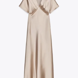 Champagnefärgad långklänning i satin från Zara - Supersnygg långklänning från Zara i champagnefärgad satin med v-ringning och korta ärmar. Klänningen har en elegant omlott-detalj vid bysten och ett flowy fall. Storlek S och aldrig använts! 