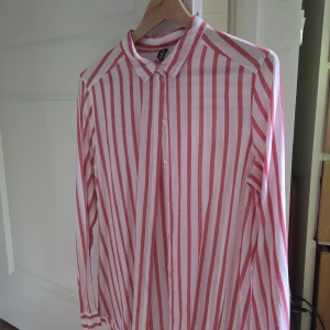 Randig skjorta  - Säljer en vit och röd randig skjorta från H&M Divided i storlek 40. Skjortan har klassisk krage, knäppning framtill och långa ärmar. Perfekt för dig som gillar en färgstark och trendig look.